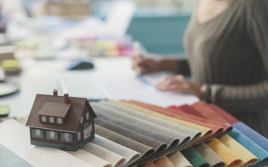 Interior designer sitting at desk and working, fabric swatches and model house in the foreground, selective focus