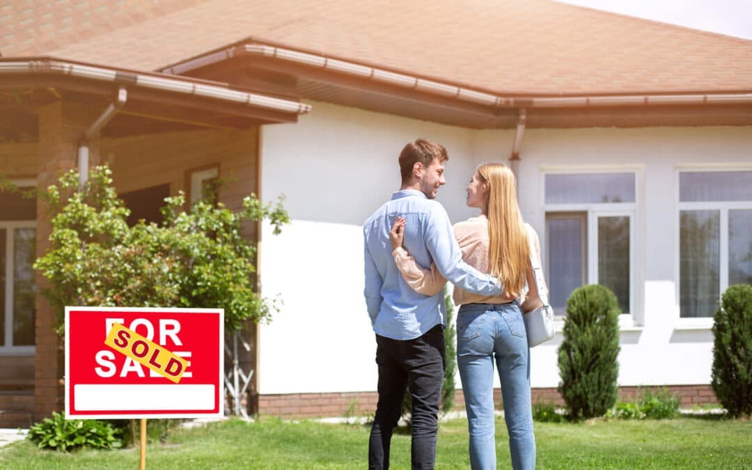 couple standing in front yard with sold sign next to them